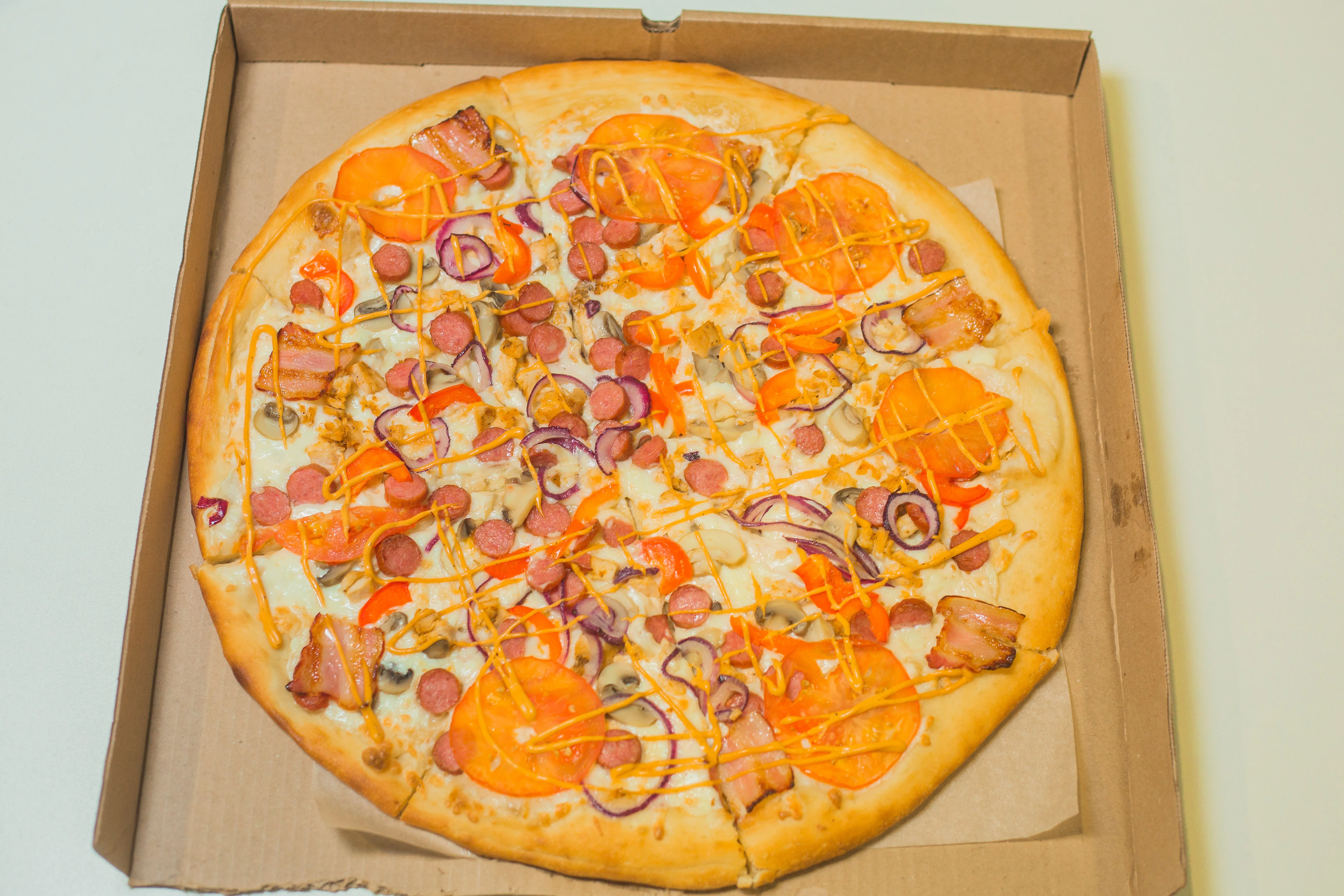 Пицца с колбасками, помидорами, беконом и другими начинками